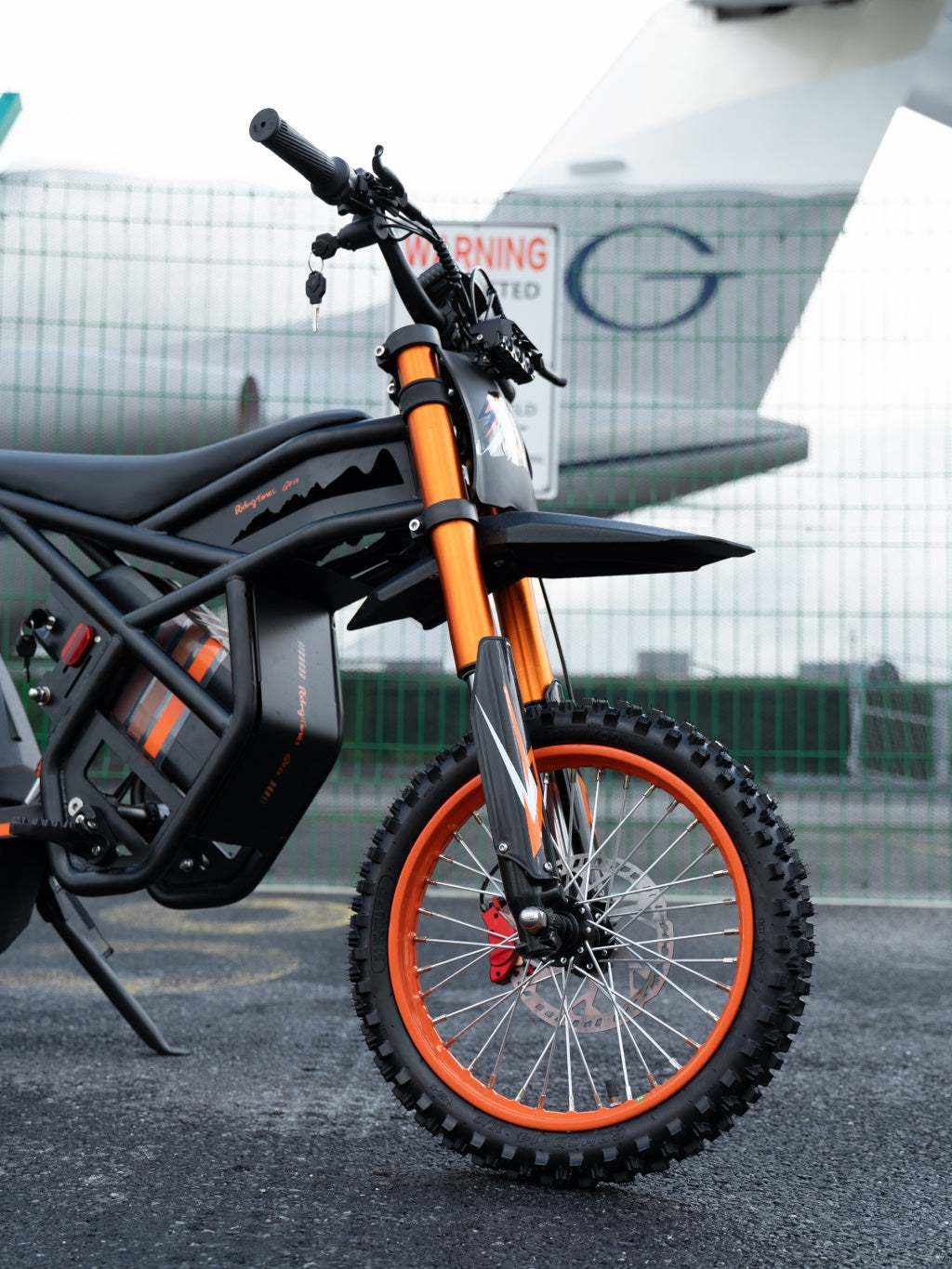 GT54 Electric Mini Motorbike featuring black frame and body with orange front suspension forks and an orange-spoked front wheel with knobby tire