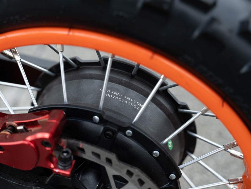Close-up of GT54 Electric Mini Motorbike wheel with bright orange rim, black motor hub, silver spokes, and red brake caliper