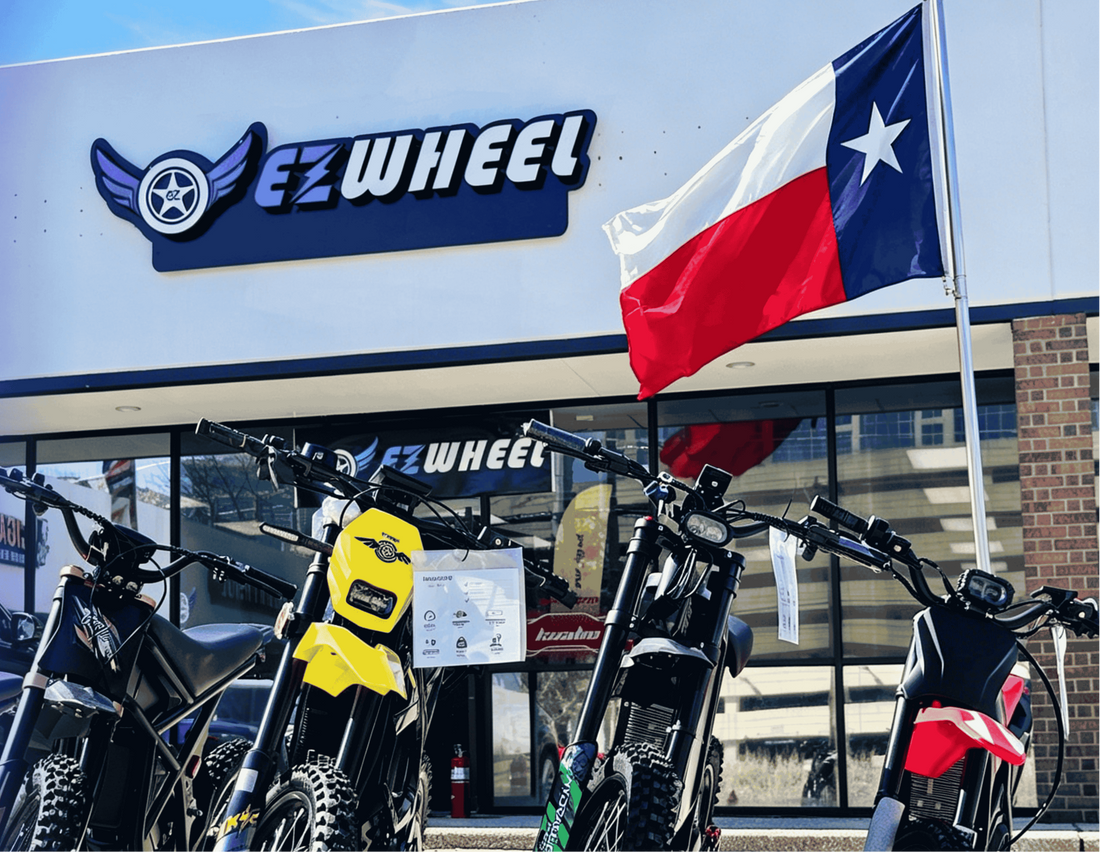 EZWheel storefront in Dallas Texas, row of off-road electric dirt bikes displayed in front of building, Texas state flag flying beside store sign, sunny day local e-bike shop photo