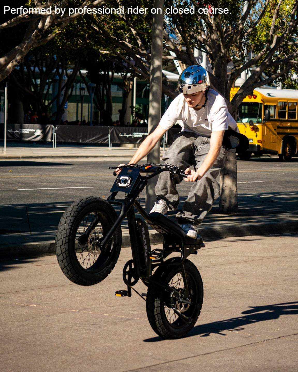 Macfox M16 electric bike in black with fat tires and front suspension performing a wheelie on an urban street