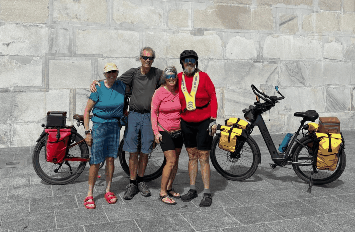 Velotric Discover 3 electric bike with black frame and yellow pannier bags parked beside four senior cyclists in casual and biking attire