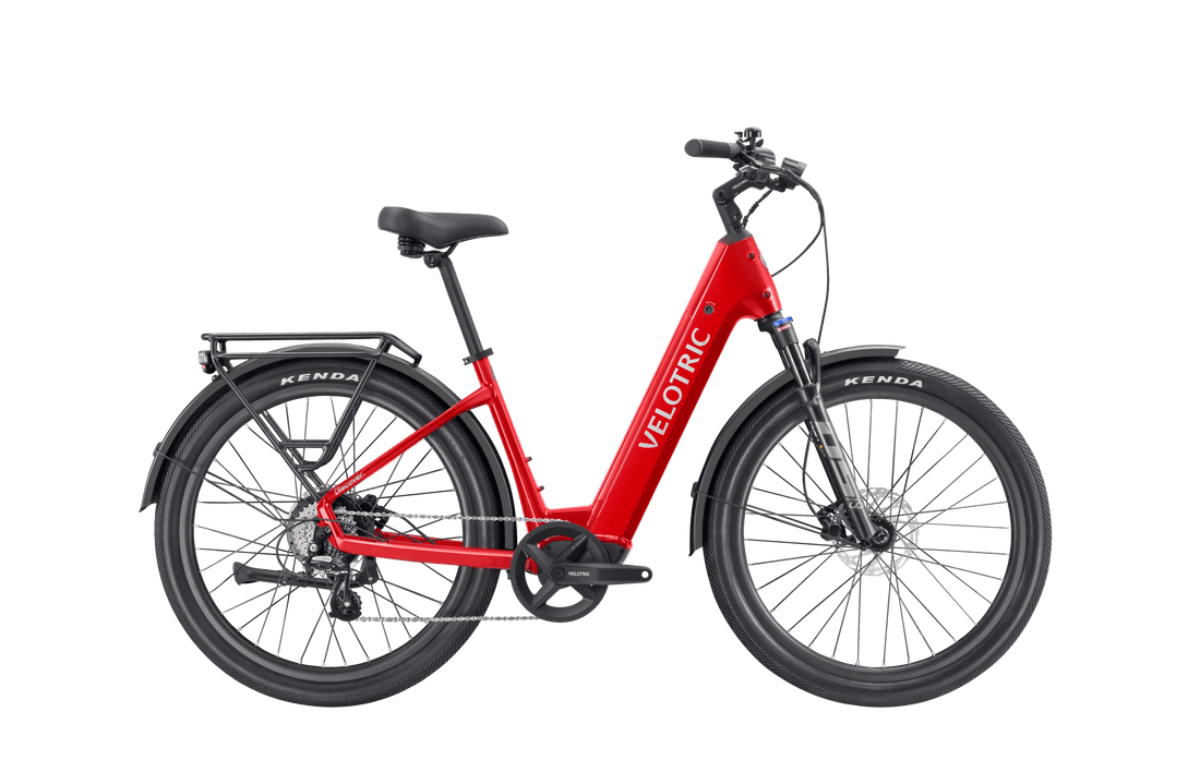 Velotric Discover 3 electric bike in olive green with tan tires, step-through frame, rear rack, and hydraulic disc brakes