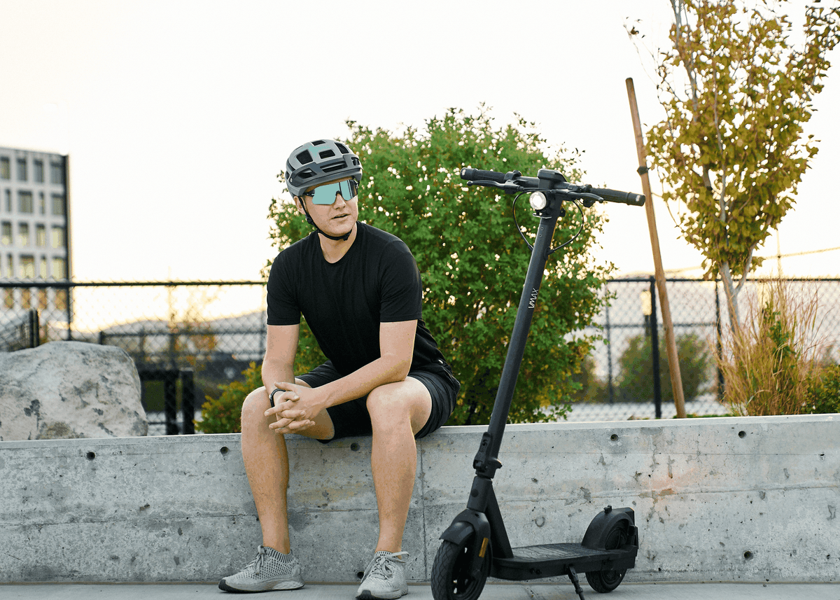 Electric scooter VMAX VX2 Hub in black with compact design and visible front headlight parked beside man wearing black outfit and helmet