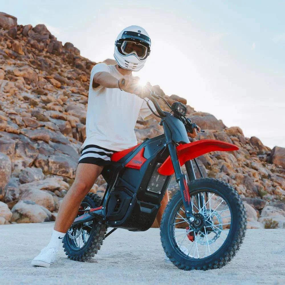 Yozma IN-10 Electric Dirt Bike in black and red with knobby off-road tires, rider wearing white helmet and casual attire